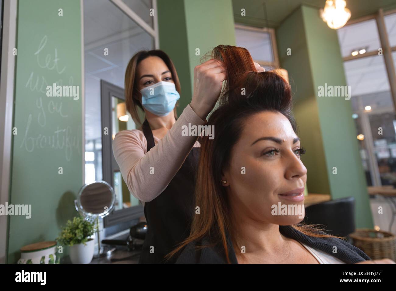 Kaukasische weibliche Friseurin, die im Friseursalon mit Gesichtsmaske arbeitet und Haarrollen auf die Haare legt Stockfoto