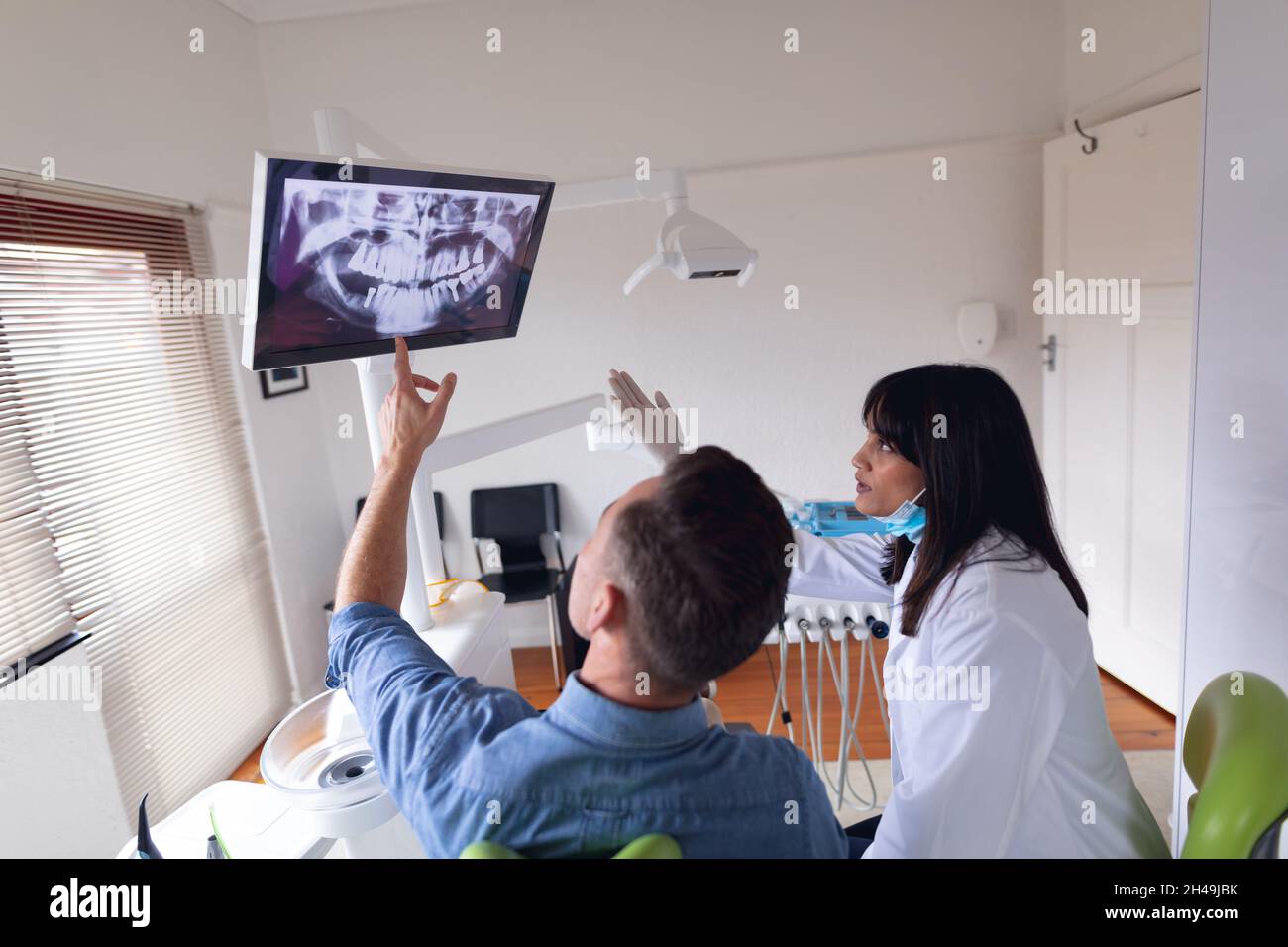 Biracial weibliche Zahnarzt trägt Gesichtsmaske Untersuchung der Zähne von männlichen Patienten in der modernen Zahnklinik Stockfoto