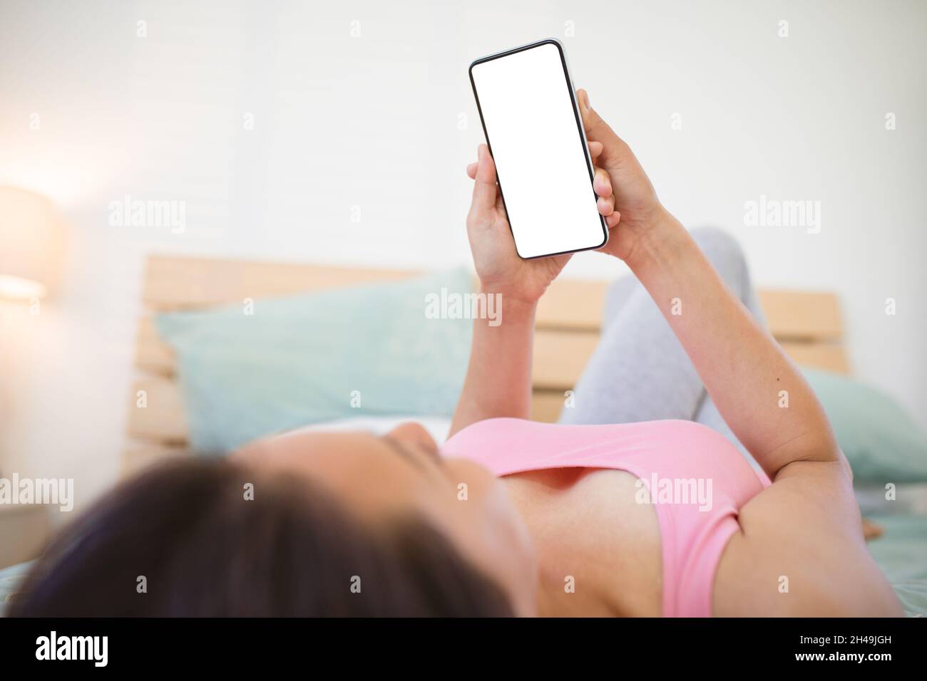 Asiatische Frau, die auf dem Bett liegt und das Smartphone mit Kopierplatz auf dem Bildschirm benutzt Stockfoto