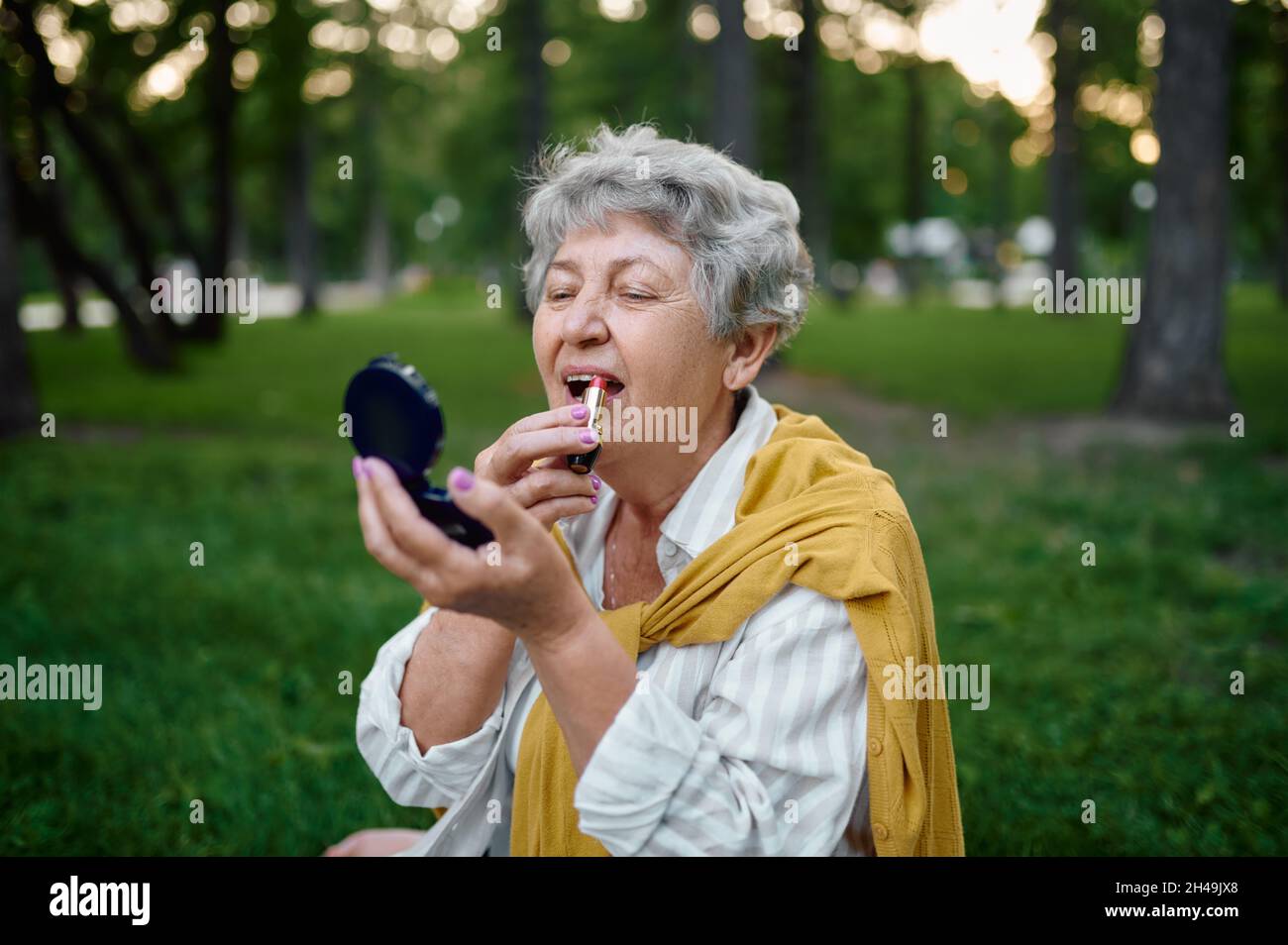 Hübsche Oma macht Make-up im Park, zurück zu yout Stockfoto