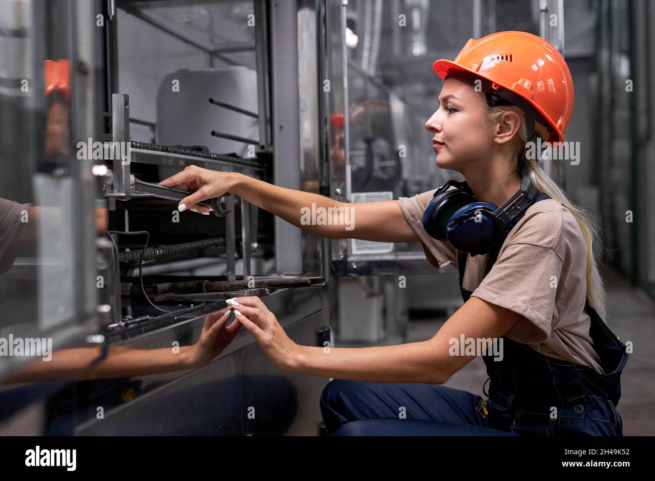 Erfahrene Frauen reparieren defekte Ausrüstung in der Fabrik mit Schraubenschlüssel, Frau in Uniform und Hardhat konzentriert sich auf die Arbeit, sieht zuversichtlich und pro Stockfoto