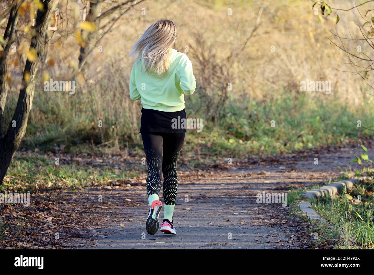 Blonde Mädchen läuft im Herbst Park auf Bäumen Hintergrund, Rückansicht. Allein Läufer, Konzept des Trainings, Abnehmen in der kalten Jahreszeit Stockfoto