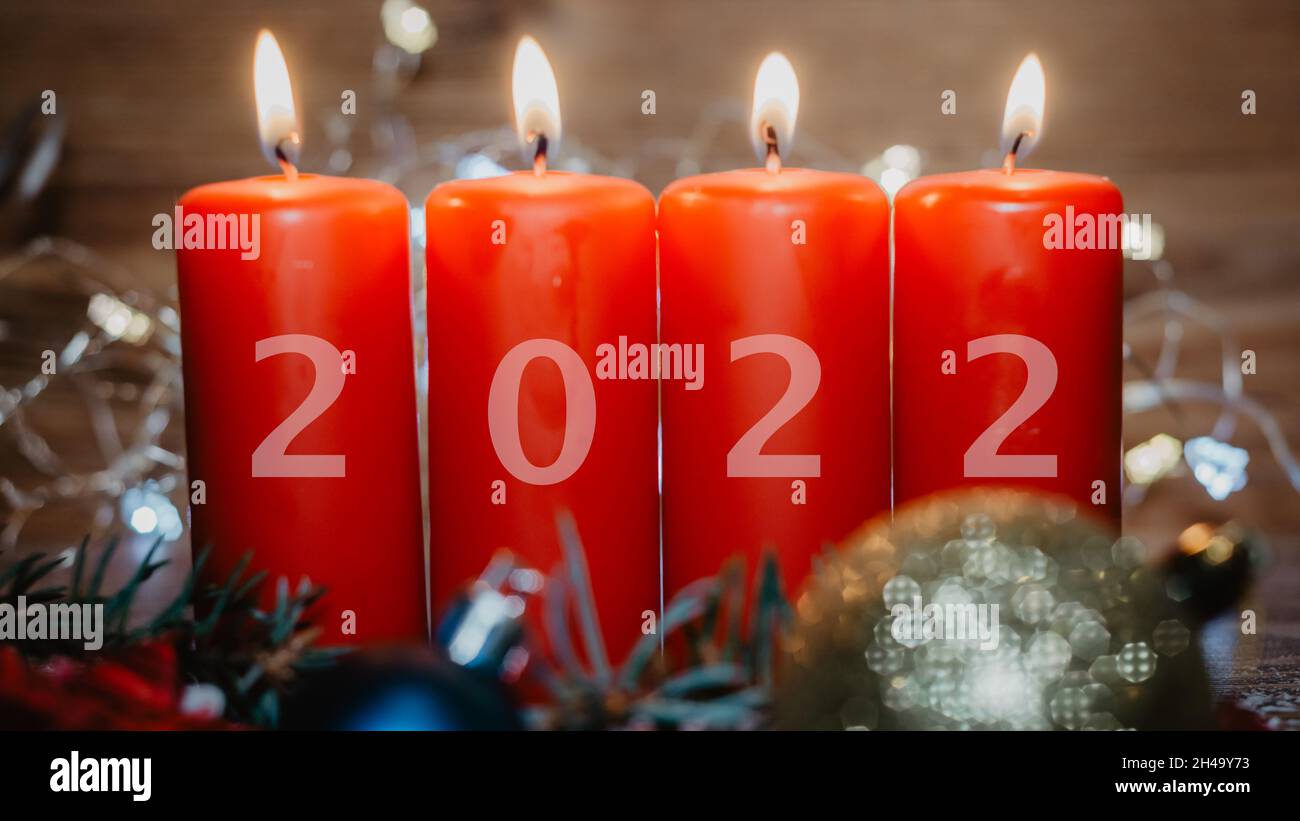 Vier rote Adventskerzen mit 2022 Figuren darauf und Weihnachtsschmuck liegen als Vorlage im Schnee Stockfoto