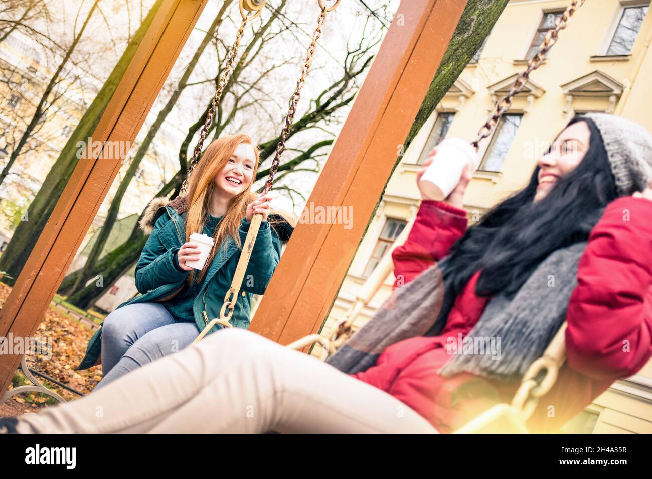 Glückliche Freundinnen mit Spaß auf Schaukel Spiel im Park in der Herbstsaison - Freundschaftskonzept mit fröhlichen Mädchen teilen Winterzeit zusammen Stockfoto