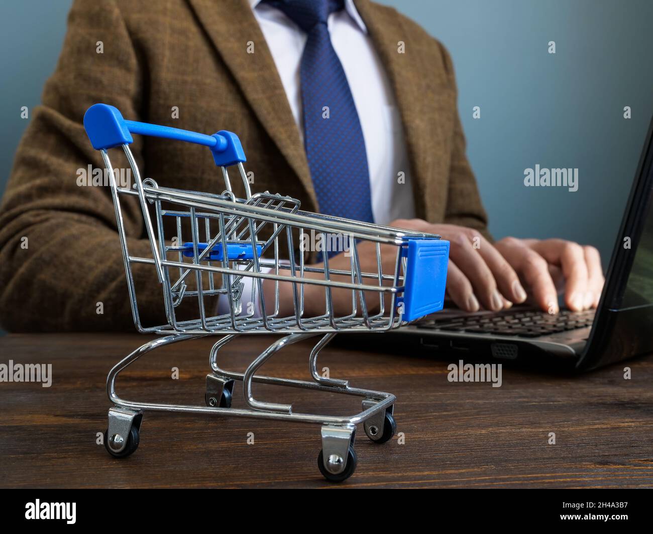 Online-Geschäftskonzept. Manager arbeitet mit einem Laptop und einem kleinen Einkaufswagen. Stockfoto
