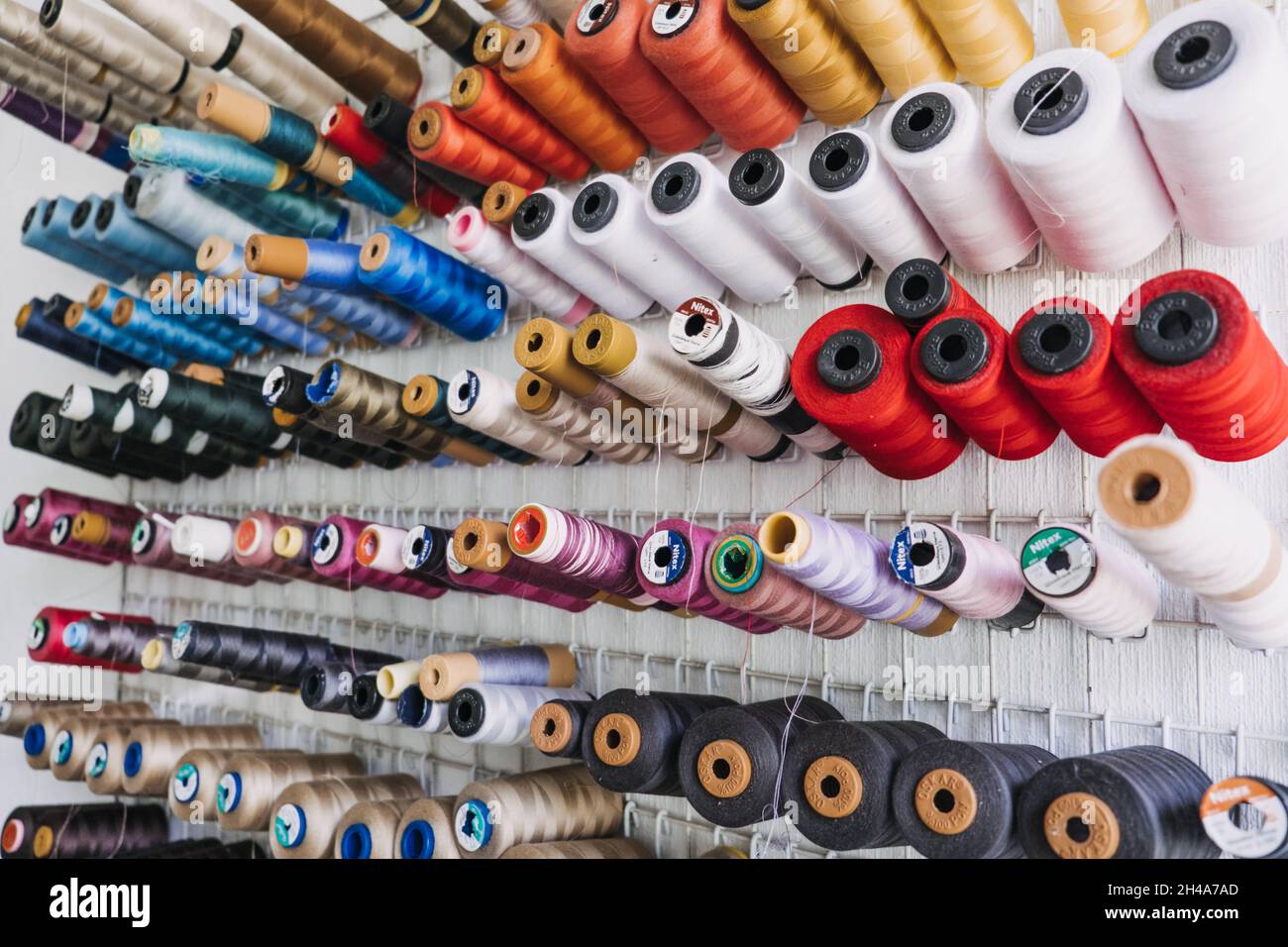 Viele Fadenspule, Baumwollgarnrolle, Nähmaterial an der Wand im Schneideratelier, Stoff. Bunte Stickerei Fadenspule im Nähstudio Stockfoto