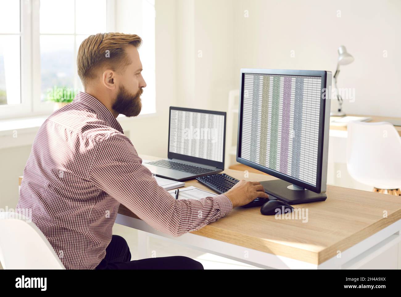 Buchhalter sitzt an seinem Schreibtisch und arbeitet mit Daten auf mehreren Computern Stockfoto