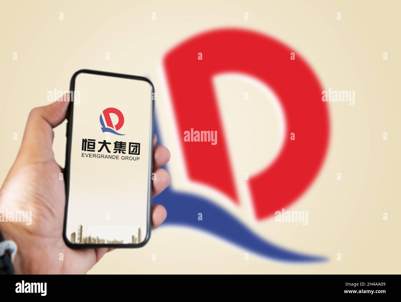 Guangzhou, China, Oktober 2021: Hand hält ein Telefon mit dem Evergrande-Logo auf dem Bildschirm und das Logo im Hintergrund verschwommen. Evergrande ist das Stockfoto