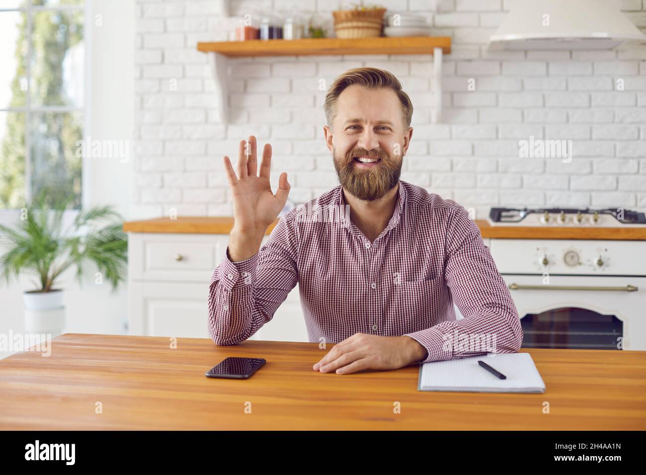Freundlicher, fröhlicher Mann, der seine Hand vor der Webcam schwenkt und den Kunden bei einem Online-Meeting begrüßt. Stockfoto