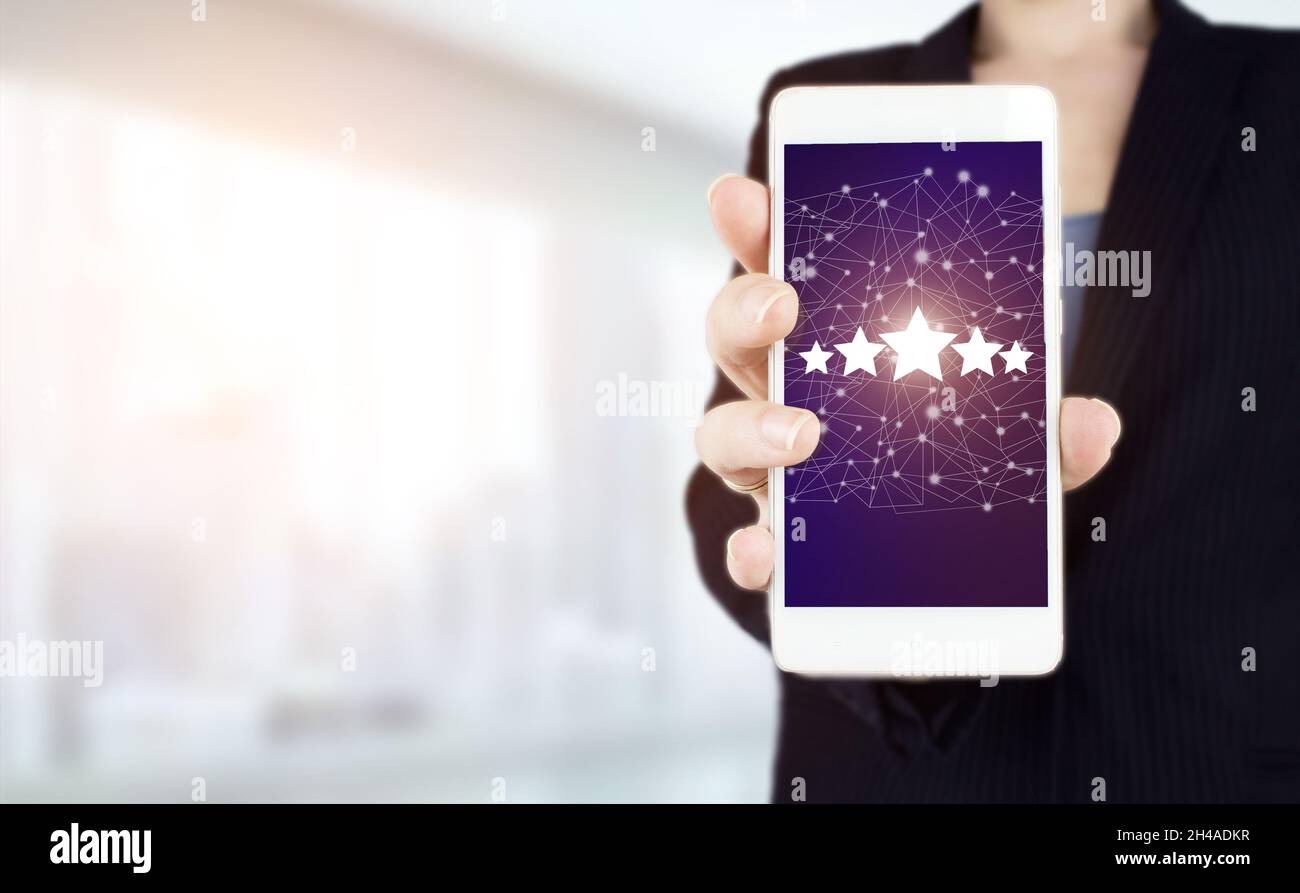 5 Sterne mit 5 Sternen und einem Bildschirm, der mit der Hand berührt wird. Handgriff weißes Smartphone mit digitalem Hologramm fünf Sterne Zeichen auf hellem verschwommenem Hintergrund. Produkt Stockfoto