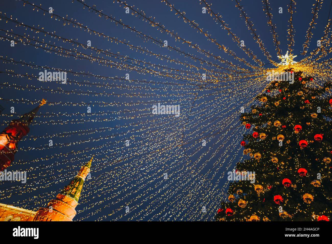 Weihnachtsbaum auf dem Roten Platz in Moskau mit goldenen Kugeln, Stern, Girlanden, funkelnden Lichtern geschmückt. Girlanden von goldenen Lichtern breiten sich von oben aus Stockfoto