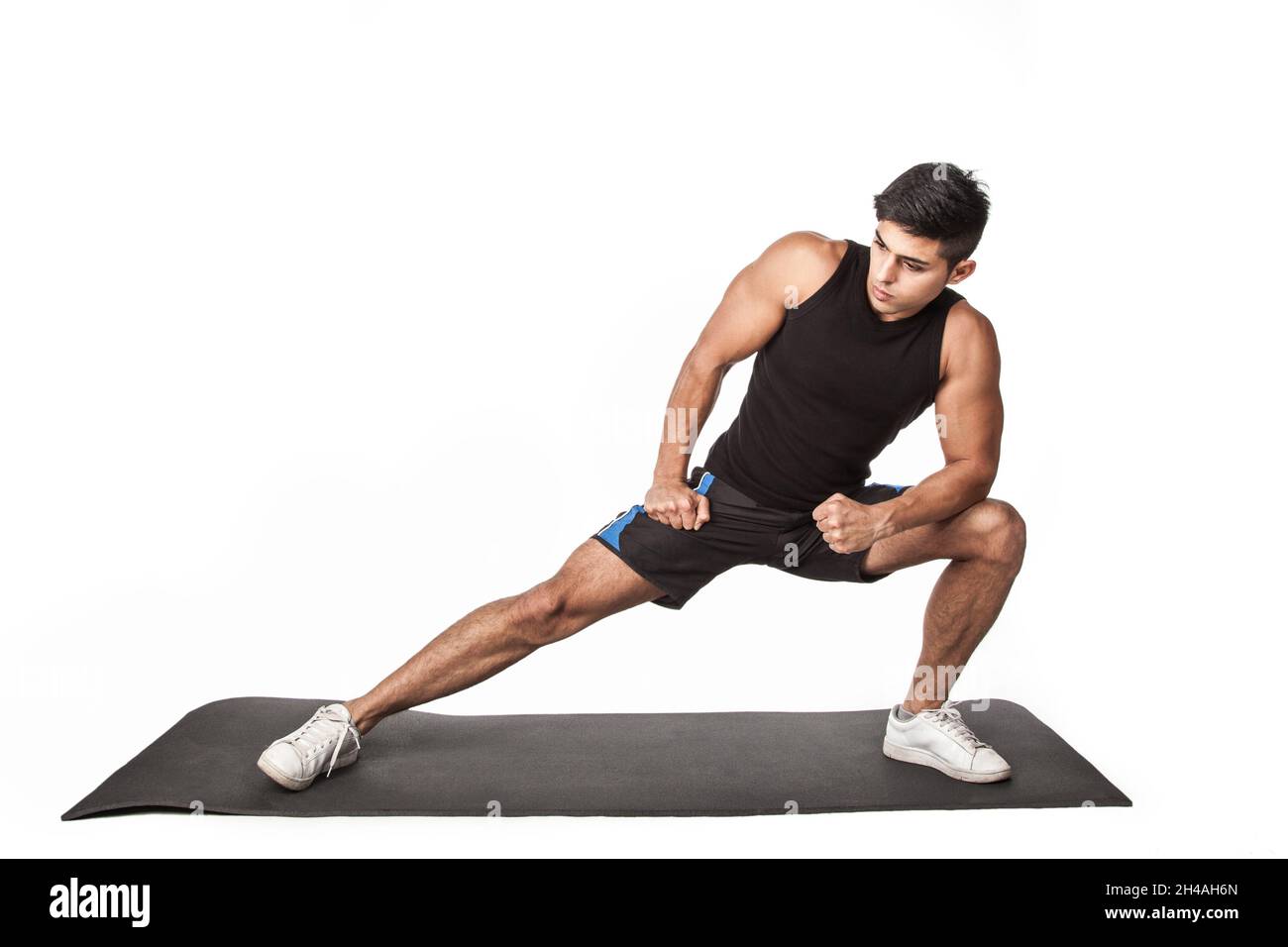 Porträt eines jungen erwachsenen Sportlers in Sportkleidung, der vor dem Training auf einer Yogamatte Beindehnungs-Übungen macht, gesunder Lebensstil. Innenaufnahme des Studios isoliert auf weißem Hintergrund. Stockfoto