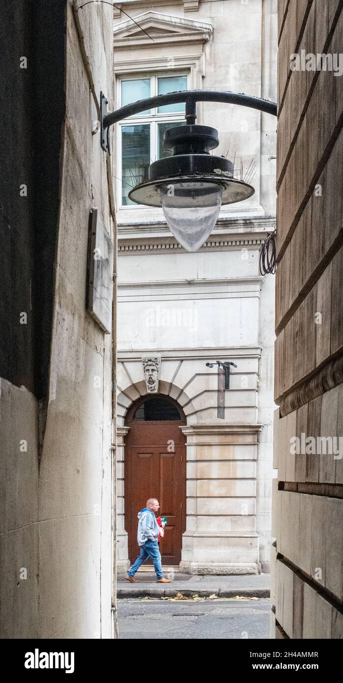 Mann, der am Ende einer engen Gasse mit einer Lampe darüber vorbeikommt, Straßenfotografie, London Stockfoto