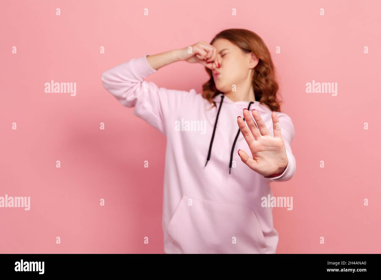 Porträt eines unangenehmen Teenagers im Hoodie Grimacing vor Ekel und Atem anhalten, Nase greifen und Stop zeigen, um stinkenden Geruch, fart Gase zu vermeiden. Innenaufnahme des Studios isoliert auf rosa Hintergrund Stockfoto