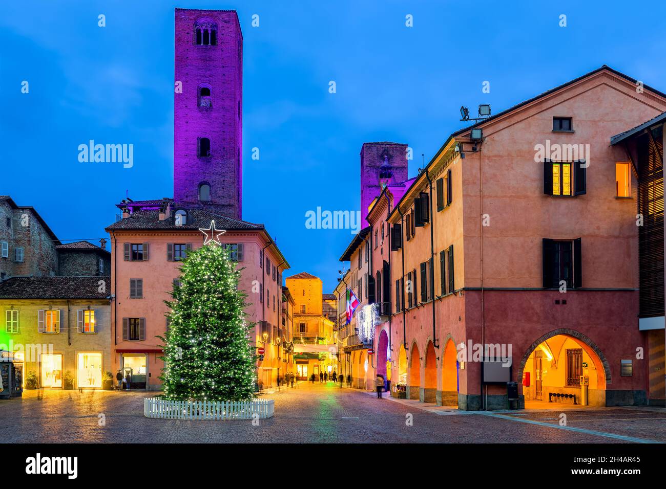 Beleuchteten Weihnachtsbaum auf dem Stadtplatz als alte mittelalterliche Türme auf dem Hintergrund am Abend in Alba, Piemont, Norditalien. Stockfoto