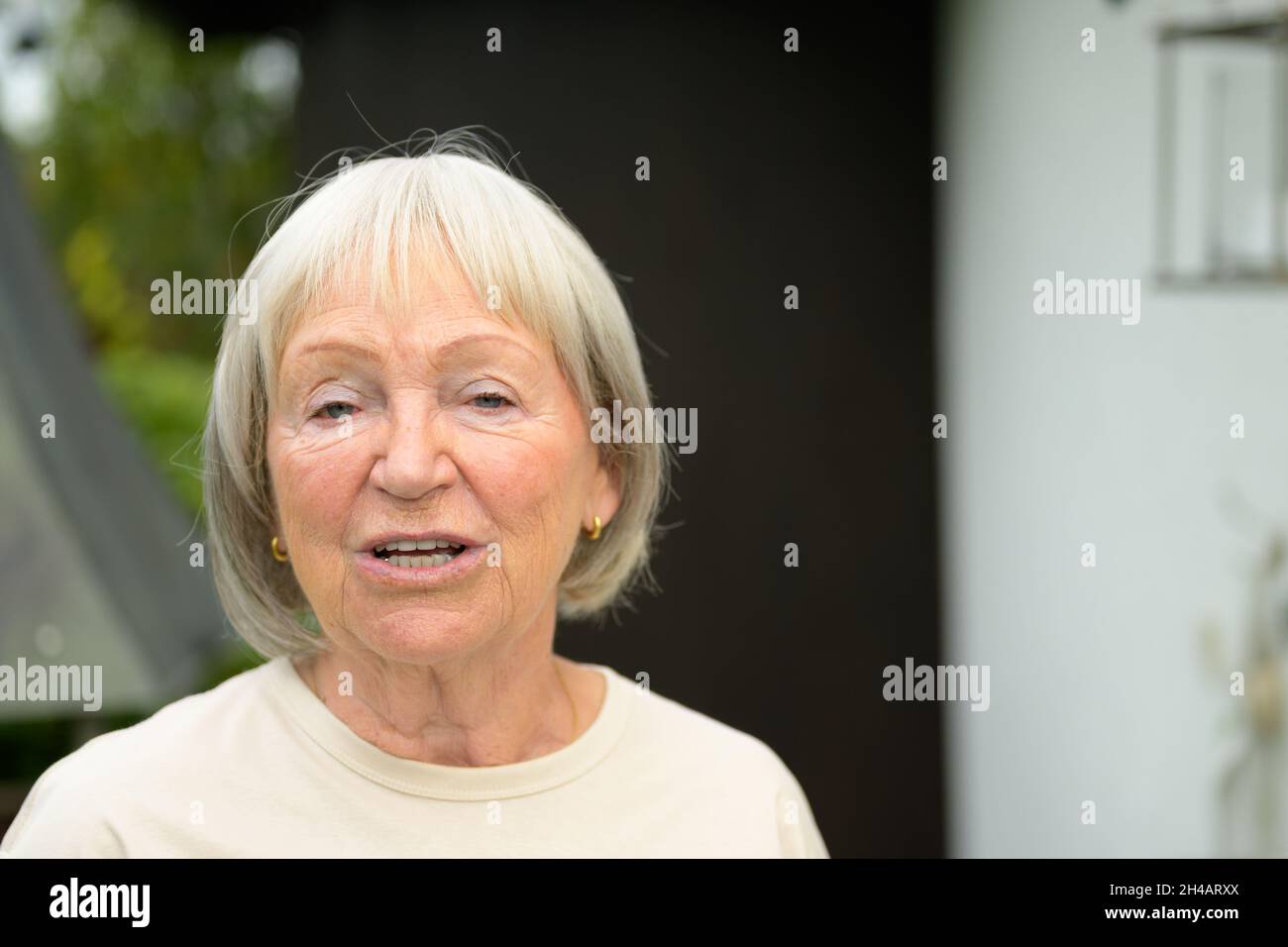 Gesprächige ältere Frau, die sich mit dem Betrachter in einem frontalen Kopf- und Schulterportrait im Freien in einem Park oder Garten unterhalten hat Stockfoto