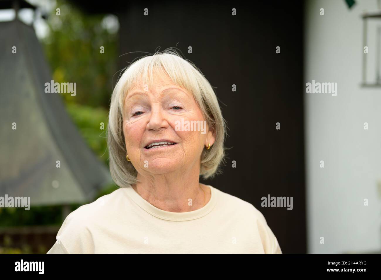 Gesprächige ältere Frau, die sich mit dem Betrachter in einem frontalen Kopf- und Schulterportrait im Freien in einem Park oder Garten unterhalten hat Stockfoto