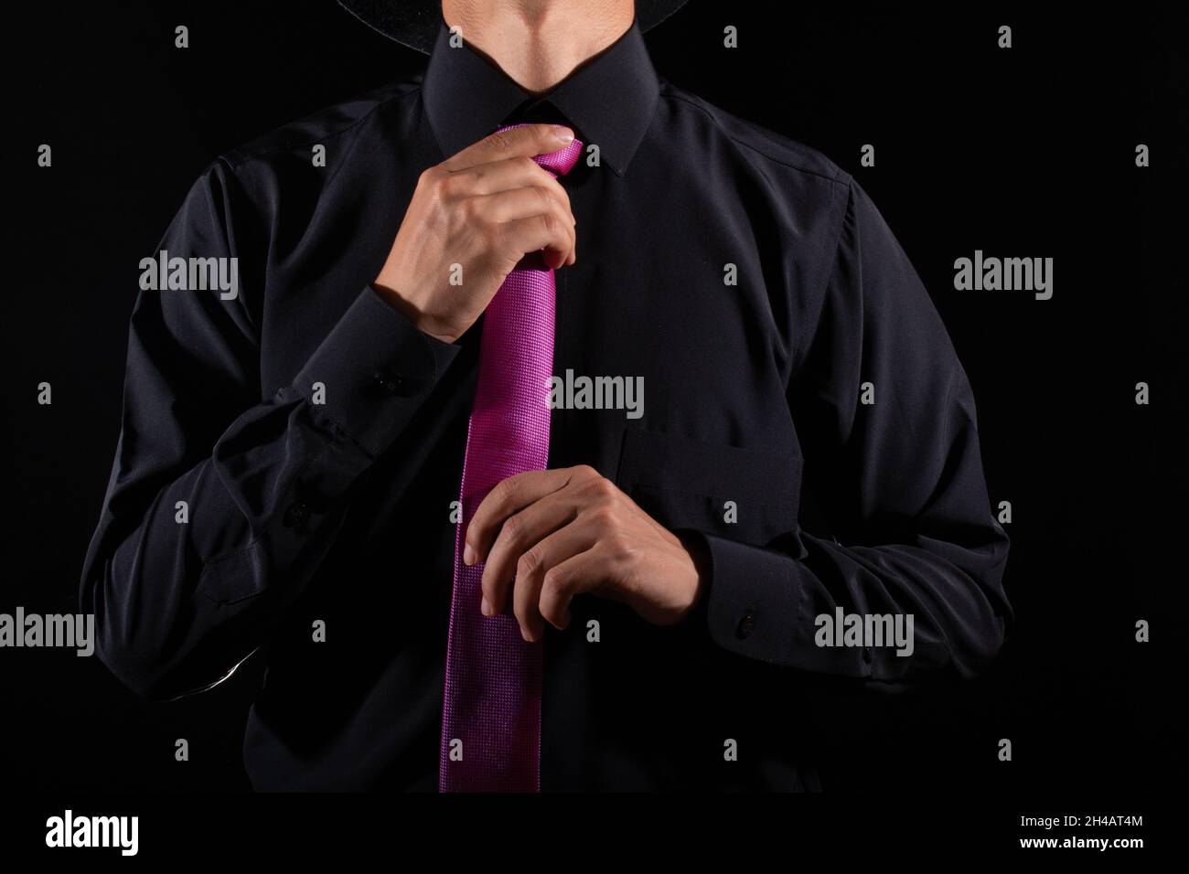 Eleganter Mann, der seine Krawatte über das schwarze Hemd bindet. Einstellen des Kabelbinders. Schwarz und violett. Junger Geschäftsmann, isoliert auf schwarzem Hintergrund. Bräutigam Stockfoto