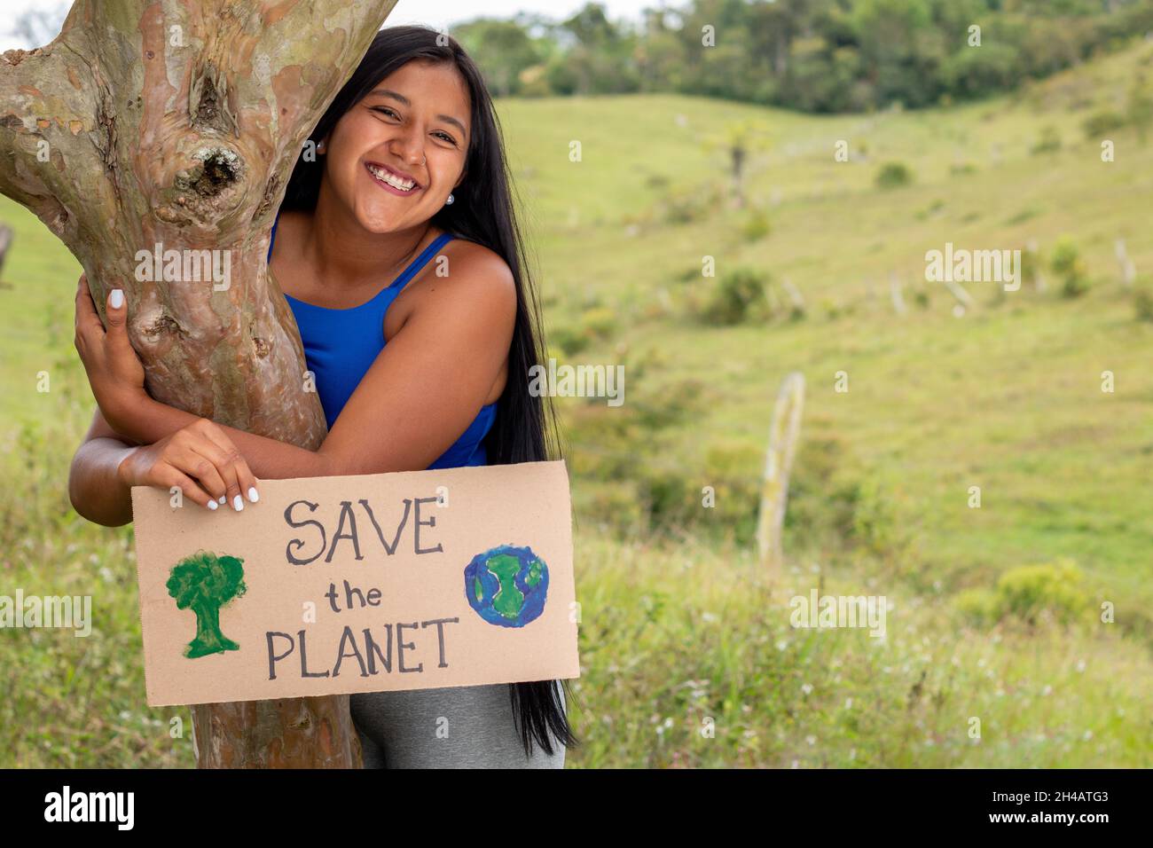 Junge Erwachsene lateinische Mädchen hält Zeichen für die Rettung des Planeten in einem tropischen Ort. Platz für Text. Brünette Frau umarmt Pflanze. Stockfoto