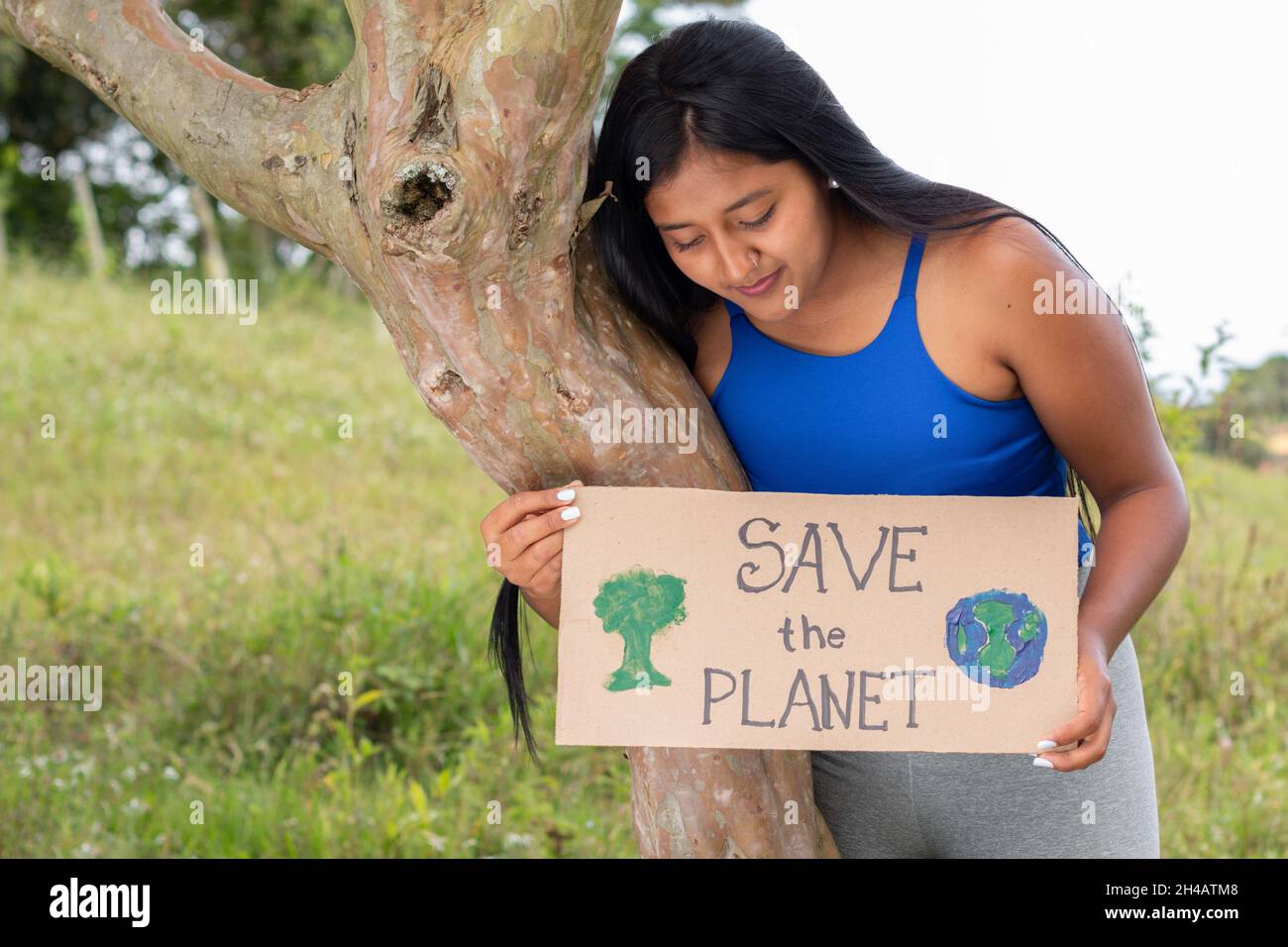 Eine Brünette hält ein Schild, das ruft, den Planeten zu retten, während sie ihn liest. Latina Mädchen schützt die Natur und Bäume. Stockfoto