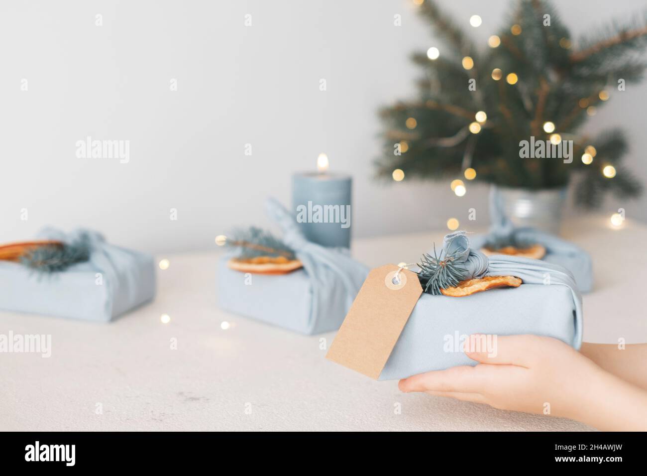 Dekoratives Weihnachtsgeschenk in umweltfreundlichem, wiederverwendbarem Stoffpaket mit Anhänger und Öko-Dekor auf einem Hintergrund von Girlanden Stockfoto