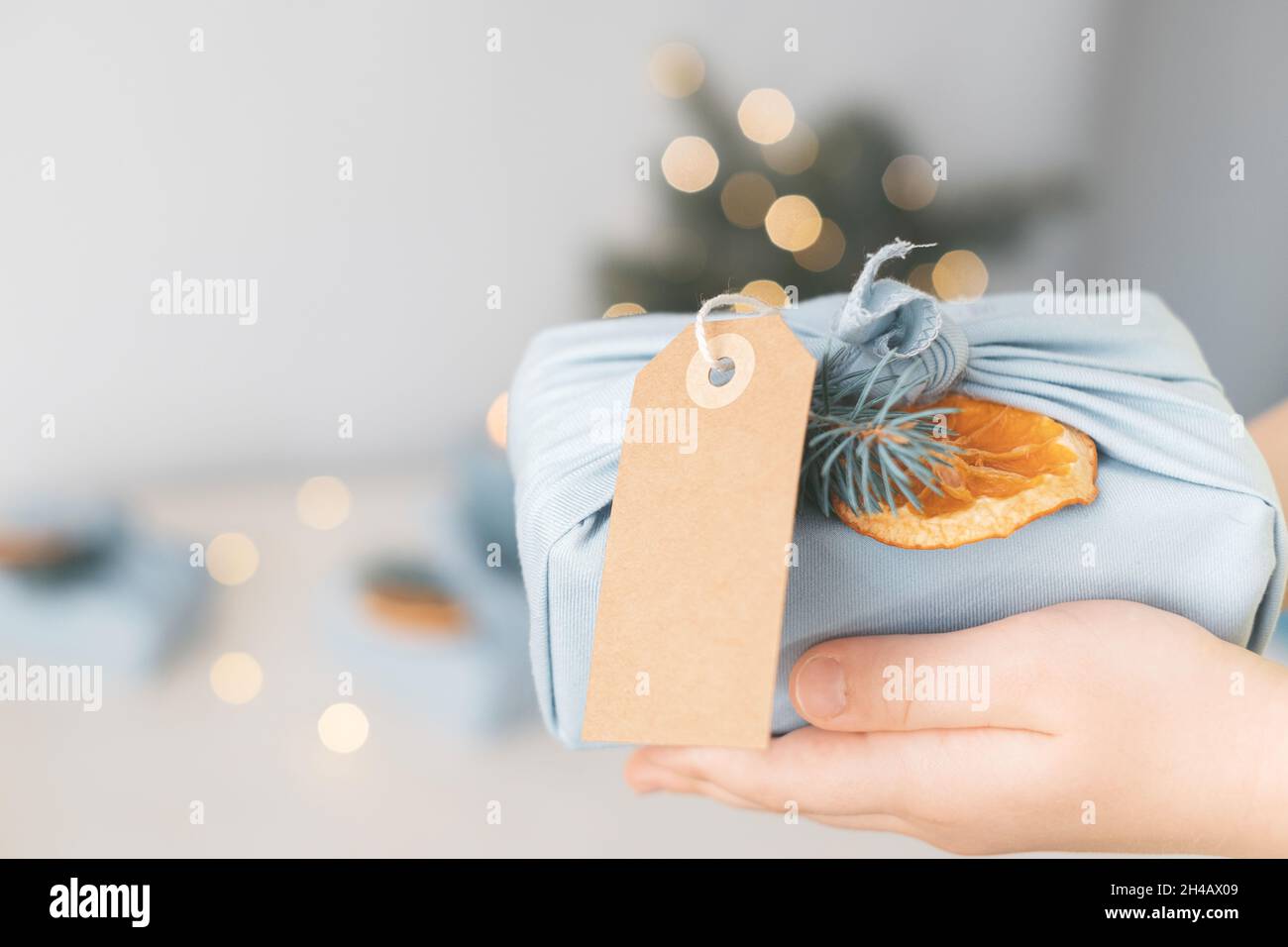 Dekoratives Weihnachtsgeschenk in umweltfreundlichem, wiederverwendbarem Stoffpaket mit Anhänger und Öko-Dekor auf einem Hintergrund von Girlanden Stockfoto