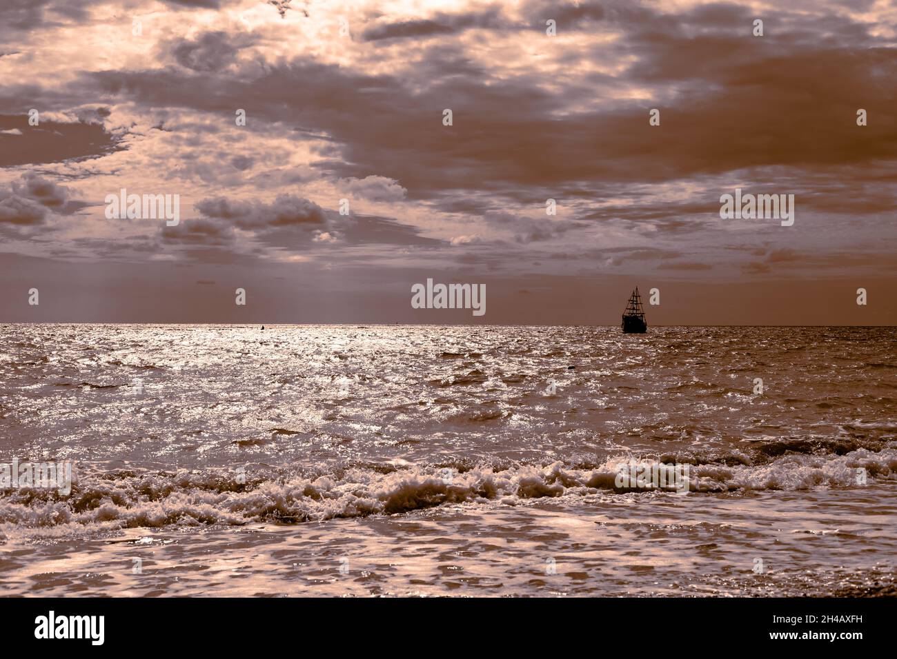 Seascape. Ein Segelschiff segelt über das glitzernde Meer vor dem Hintergrund eines dunklen Himmels, goldener Tonung. Reisen auf dem Meer Stockfoto