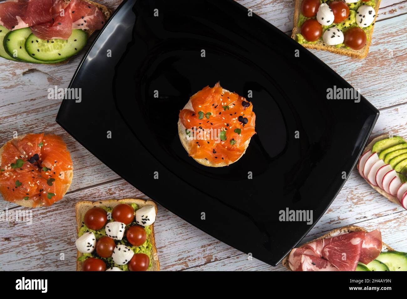 Ein Sandwich mit rotem Fisch befindet sich auf einem schwarzen Teller und es gibt viele andere Sandwiches. Stockfoto