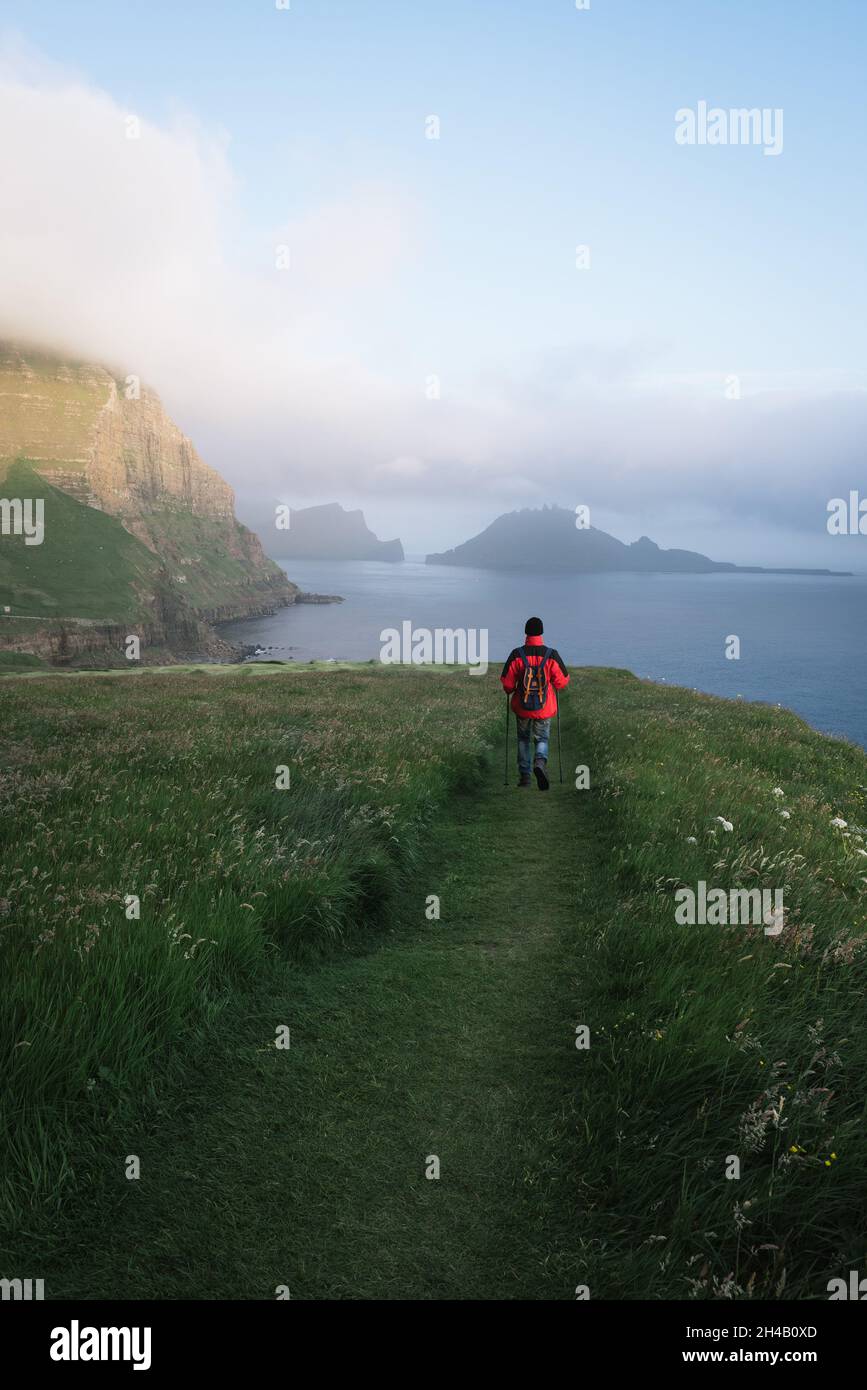 Wandern im Dorf Gaadalur, Färöer-Inseln. Ein Tourist mit Rucksack spaziert entlang des Weges auf der Insel Vagar Stockfoto