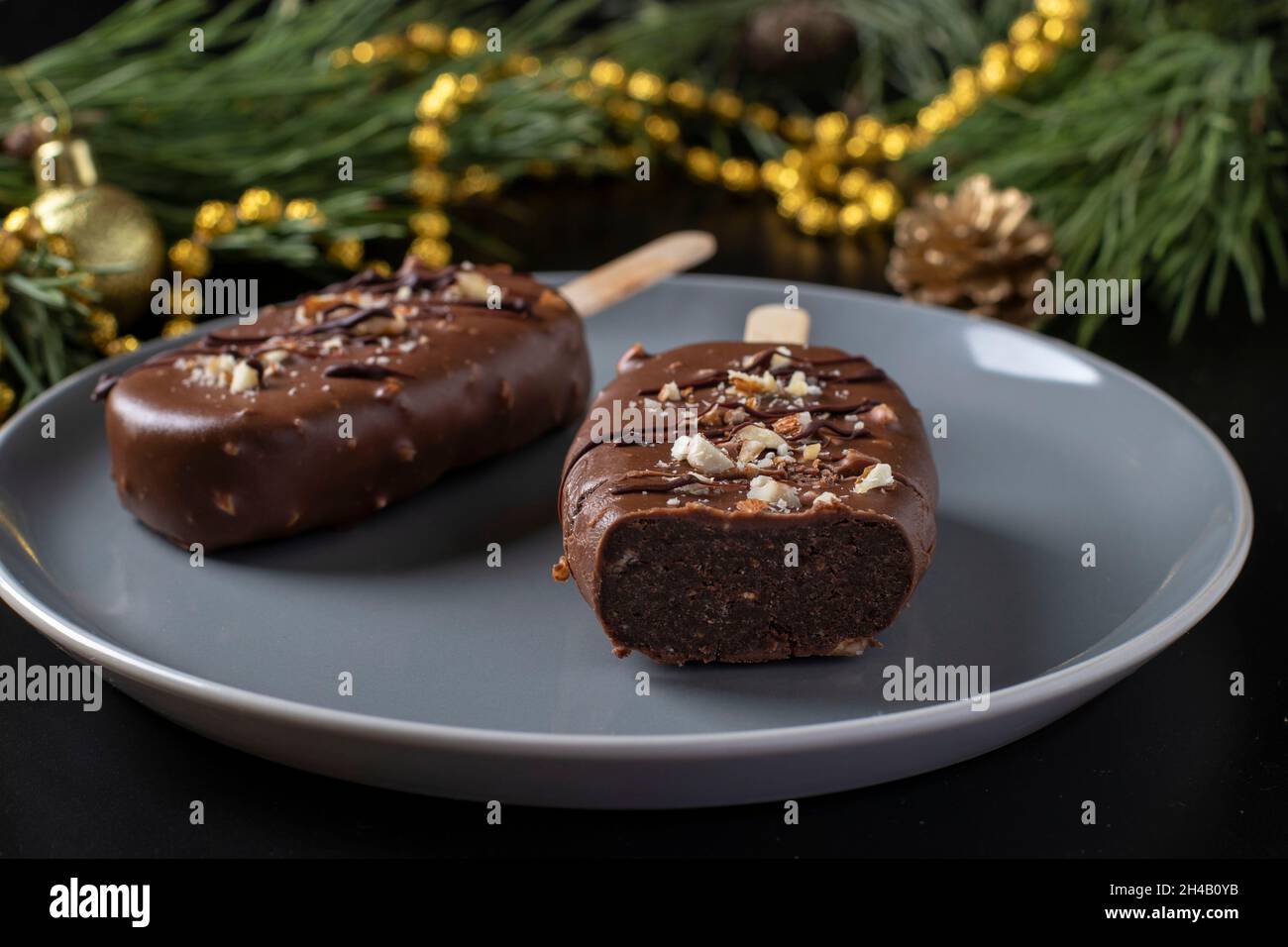 Schokoladen-Popsicle-Kuchen mit Nüssen auf einem Stock auf einem grauen Teller auf dunklem Hintergrund. Stockfoto