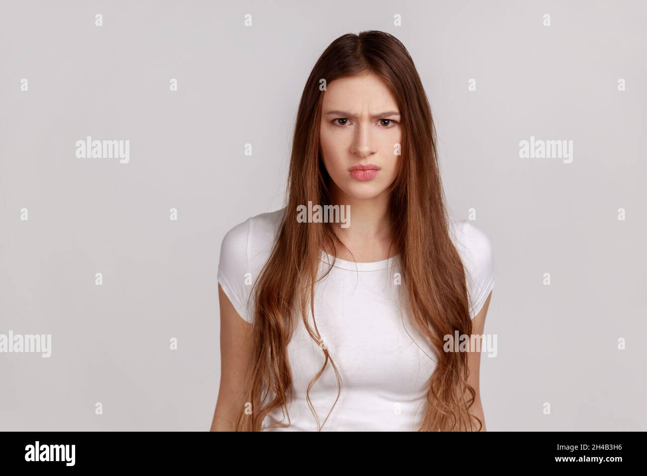 Porträt einer jungen erwachsenen Frau, die mit geballten Zähnen und wütender Grimasse im Gesicht steht und sich als aggressiv ausgibt und weißes T-Shirt trägt. Innenaufnahme des Studios isoliert auf grauem Hintergrund. Stockfoto