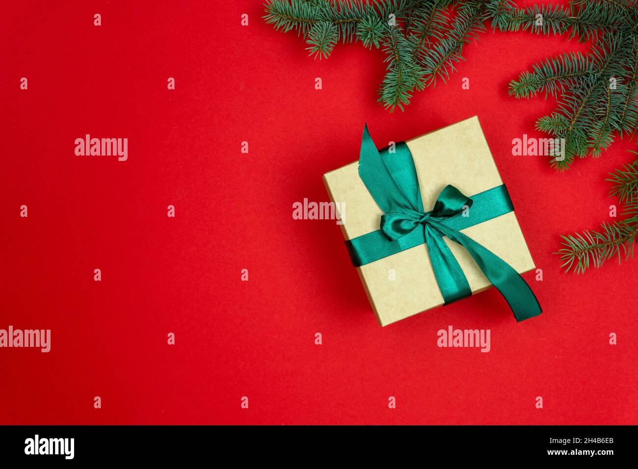 Weihnachtliche Tannenzweige auf rotem Hintergrund und Geschenkverpackung mit grüner Schleife. Das kunsthandwerklich gefärbte Geschenk ist mit einem zedigen Band gebunden. Flach liegend, Draufsicht, Kopie Stockfoto