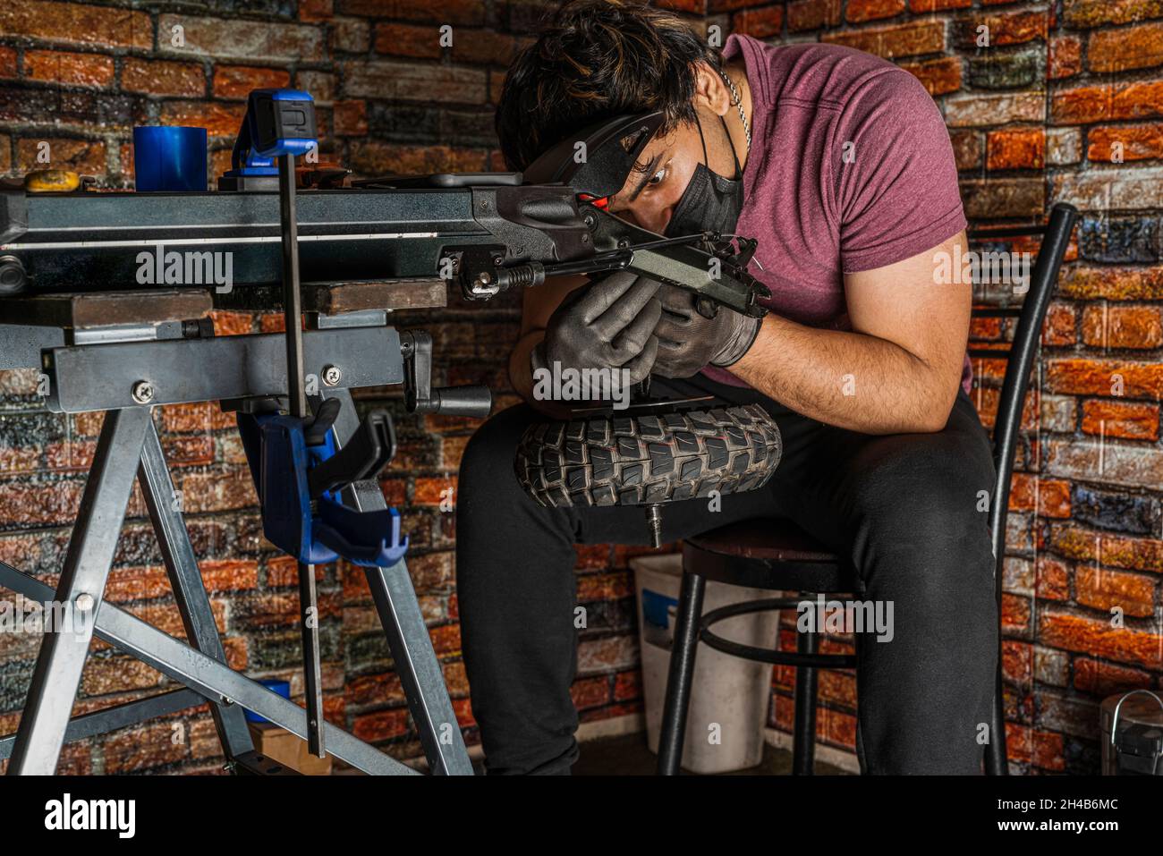 Junger erwachsener Mechaniker sitzt auf einem Stuhl und überprüft sorgfältig die Verkabelung, die zum Rad eines Elektrorollers in seiner Werkstatt geht. Stockfoto