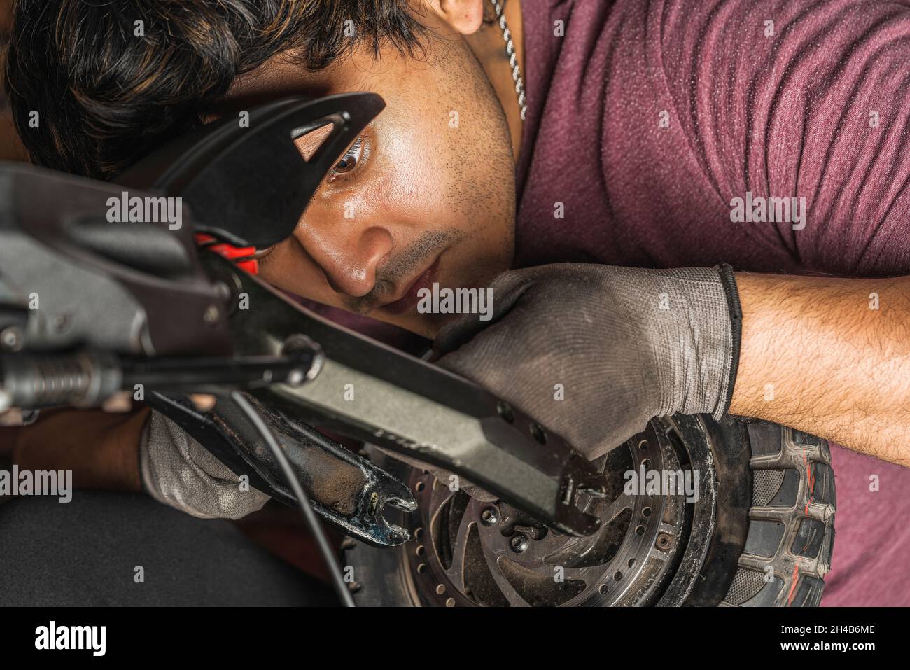 Nahaufnahme eines jungen lateinischen Mechanikers, der die Verkabelung, die zum Rad eines Elektrorollers in seiner Werkstatt geht, sorgfältig überprüft Stockfoto