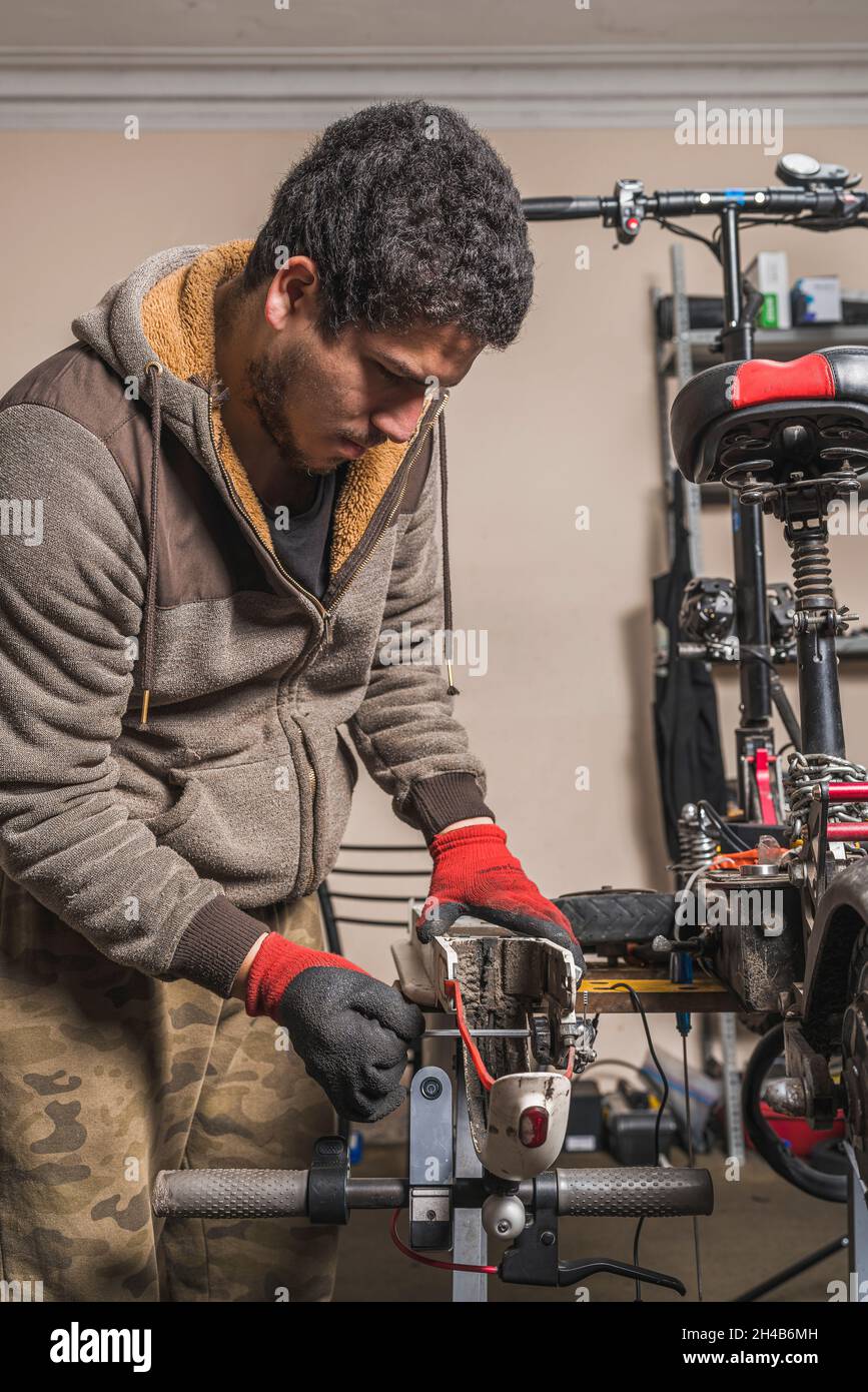 Vertikales Bild eines Mechanikers, der einen Kotflügel eines Elektrorollers auf einem Tisch in der Werkstatt repariert. Stockfoto
