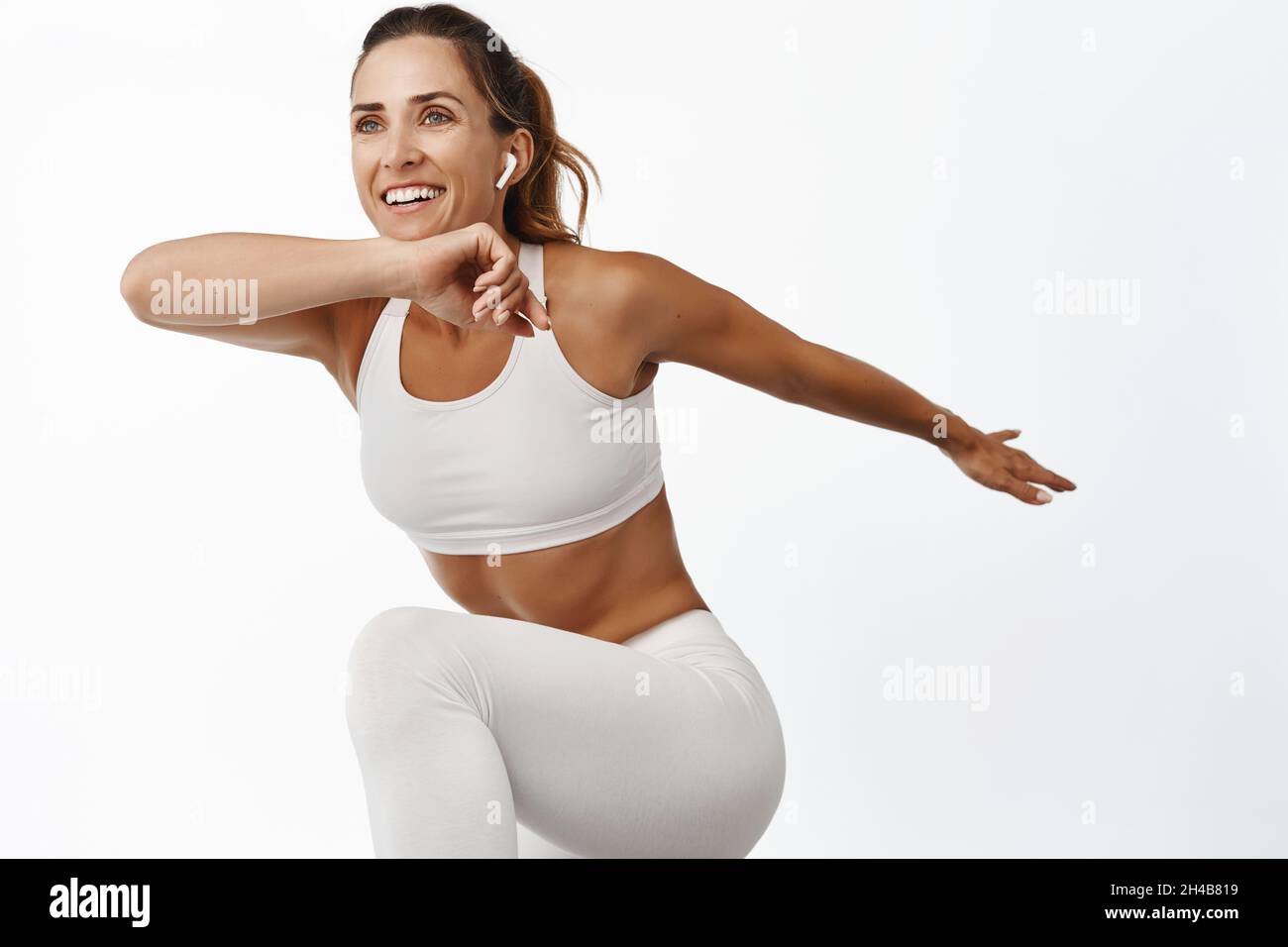 Porträt einer Sportlerin, die ihren Körper streckt, trainiert, ihr Bein hebt und lächelt, läuft, auf weißem Hintergrund steht Stockfoto