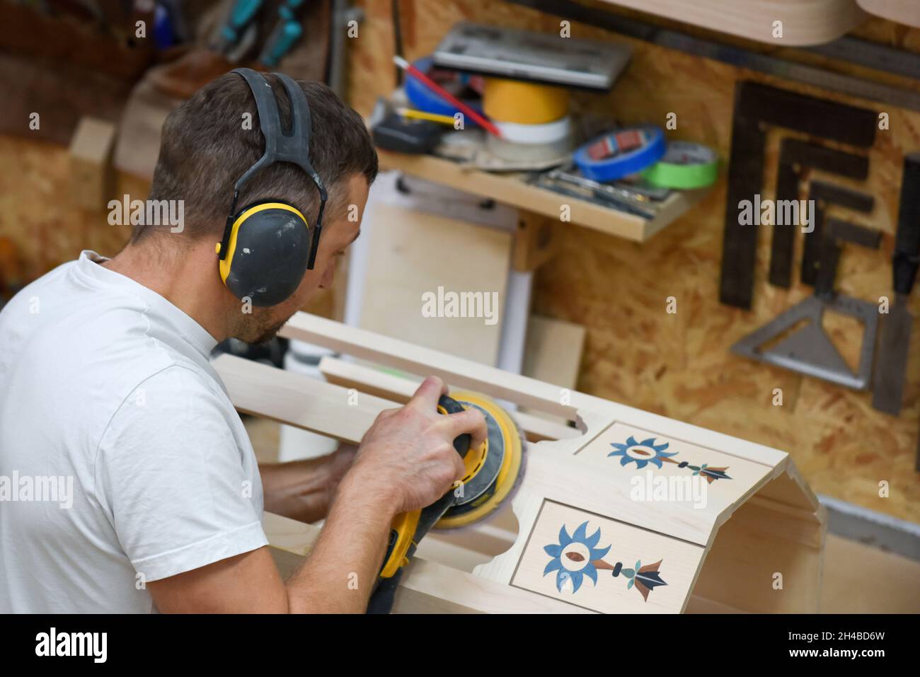 Ein Mann, der mit einem Elektroschleifer für Elektrowerkzeuge Holz in der Tischlerei basteln kann Stockfoto