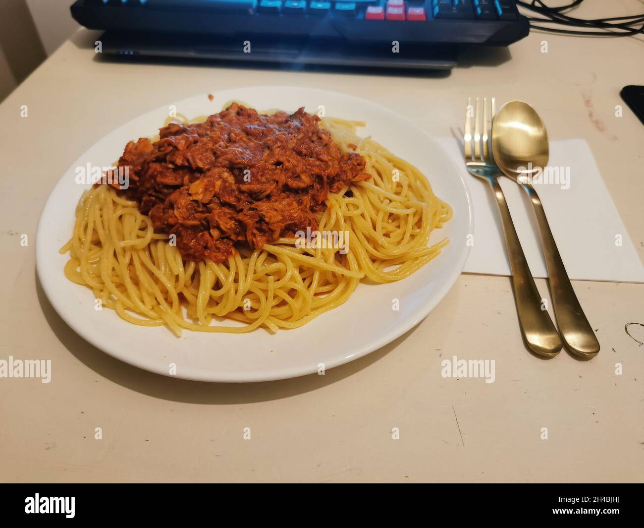 Spaghettis mit einer Sauce darauf vor einem Laptop und Besteck. Stockfoto