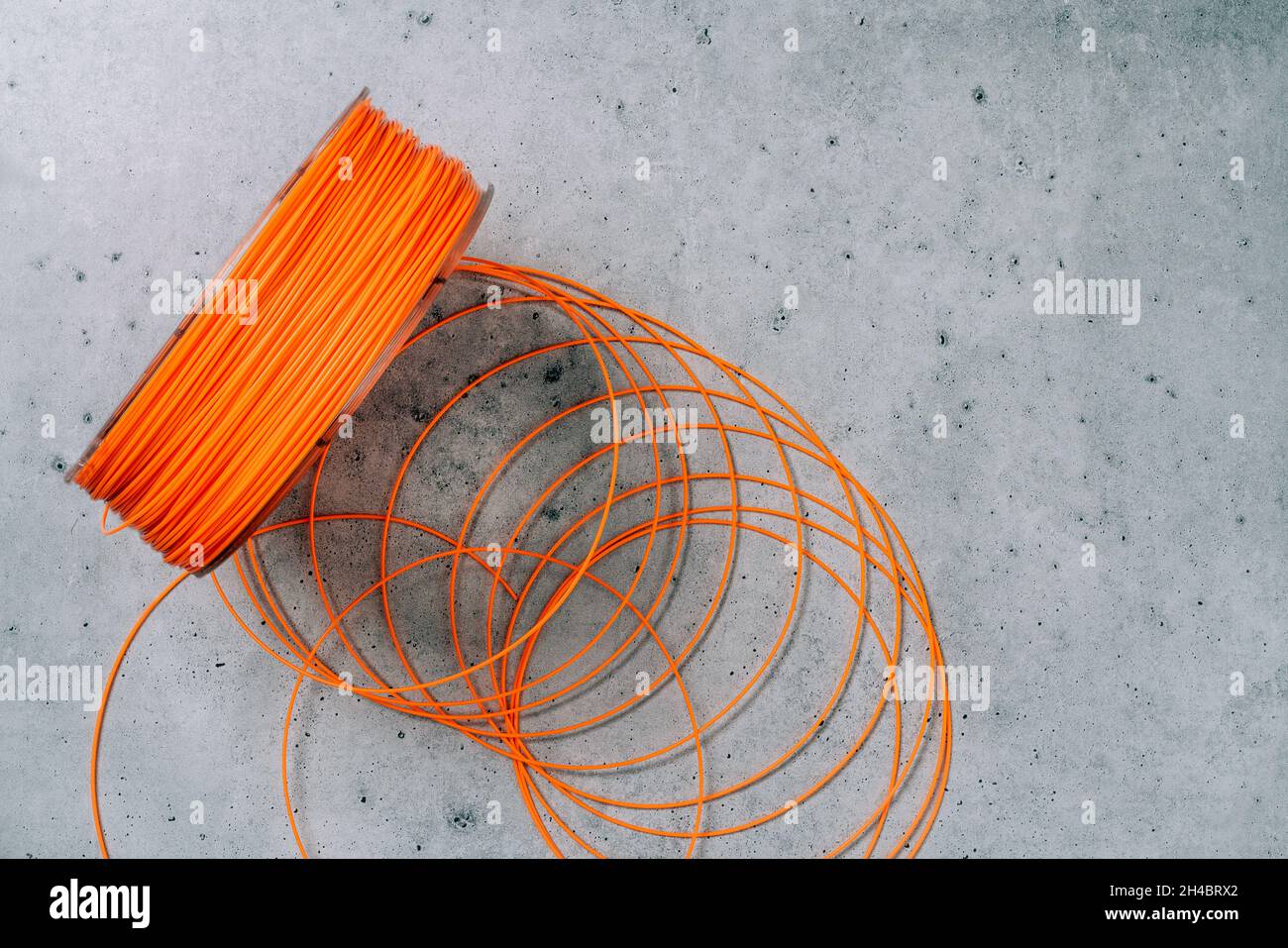 Kunststofffaden für 3d-Drucker. Spule aus orangefarbenem thermoplastischem Draht für 3D-Druck aus nächster Nähe auf grauem Steingrund, flach liegend Stockfoto