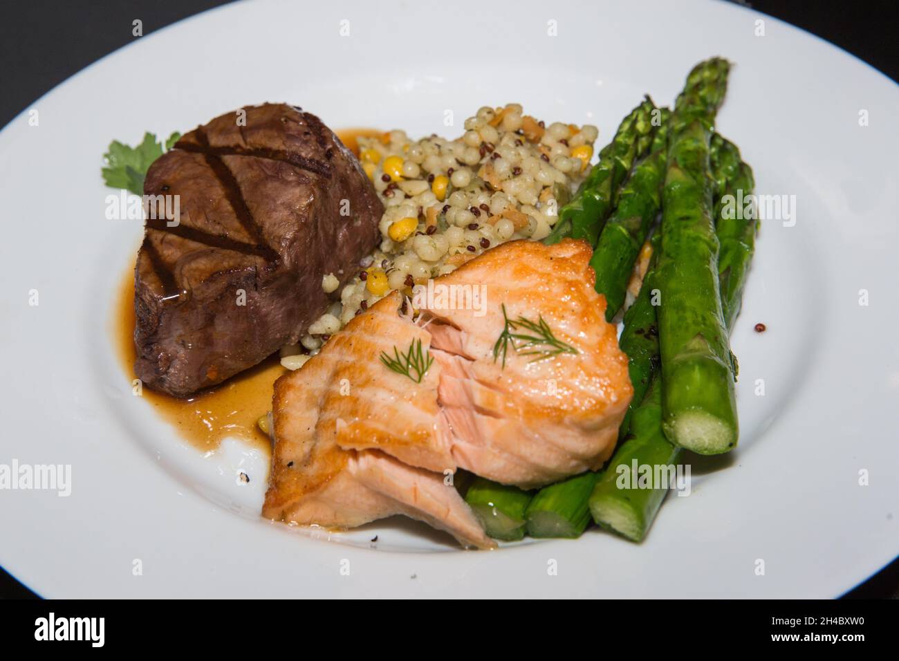 Ein Speiseteller mit Steak, gegrilltem Lachs, Kartoffelpüree und gebratenem Gemüse wird vorbereitet. Stockfoto