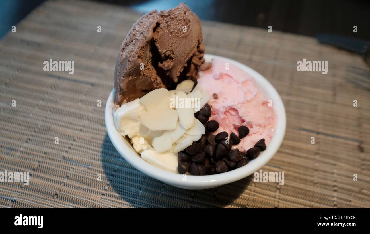 Eiscreme – Vanilleschokolade und Erdbeere mit in Scheiben geschnittenen Mandeln und Schokoladensplitter in einer Schüssel Stockfoto