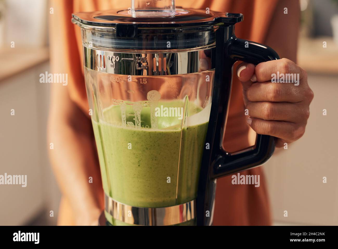 Hand der jungen Frau hält elektrischen Mixer mit frischen hausgemachten Smoothie der grünen Farbe zum Frühstück vorbereitet Stockfoto