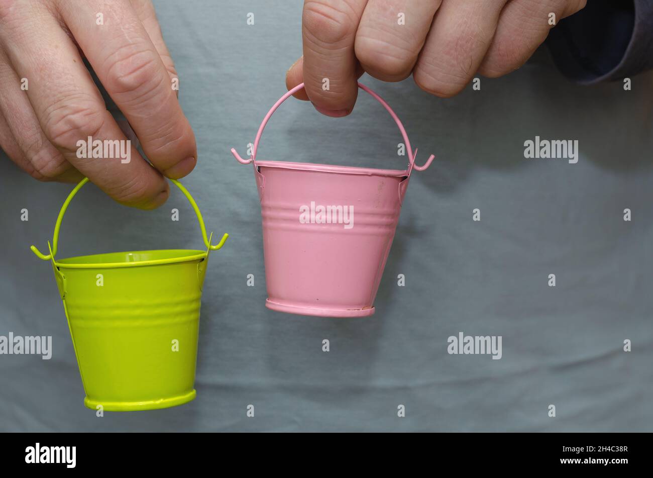 Zwei Männerhände mit Spielzeug-Eimern. Pinke und grüne Babyeimer. In Innenräumen. Selektiver Fokus. Stockfoto