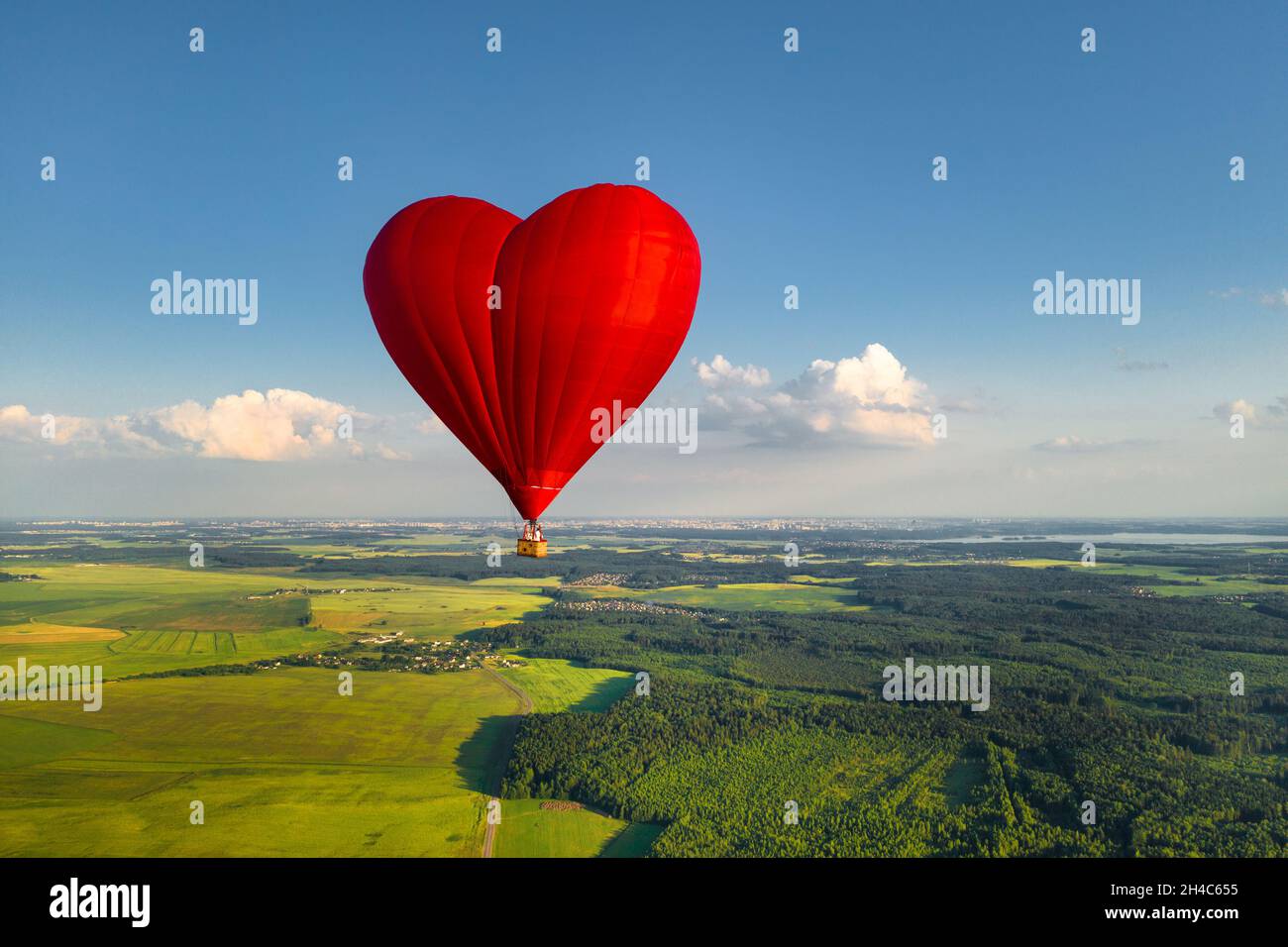 Roter herzförmiger Ballon mit Menschen über grünen Feldern und Wäldern. Stockfoto