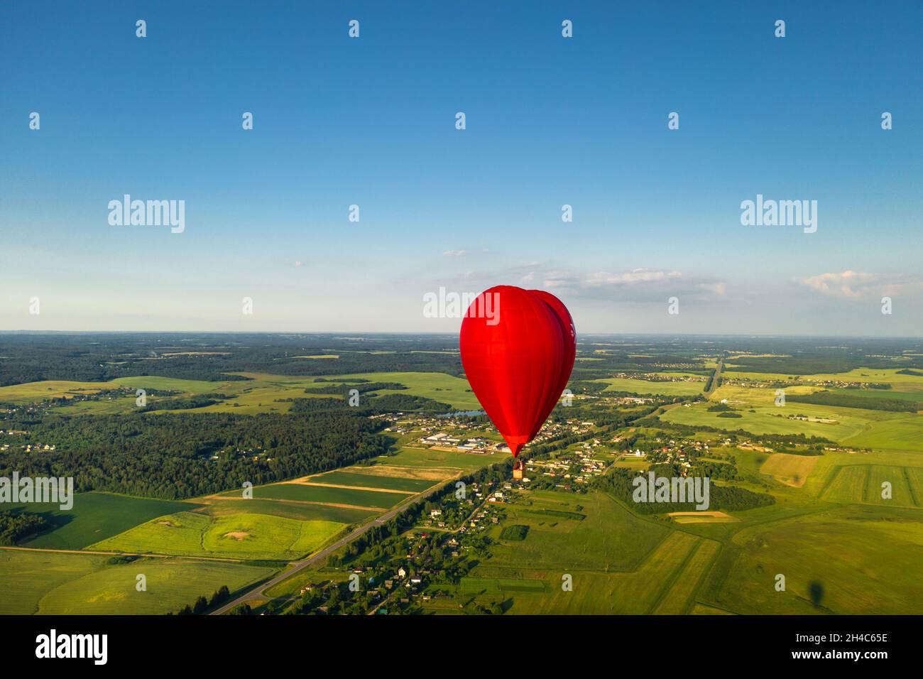 Roter herzförmiger Ballon mit Menschen über grünen Feldern und Wäldern. Stockfoto