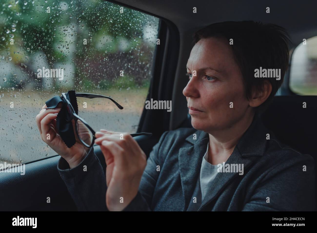 Geschäftsfrau reinigt Brillen auf dem Rücksitz eines Autos bei Regen, selektiver Fokus Stockfoto