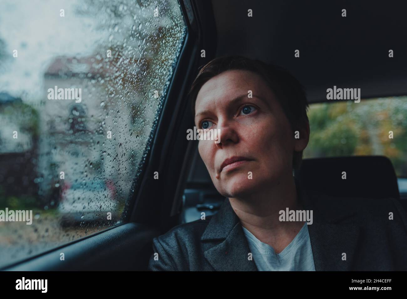 Besorgte Geschäftsfrau, die im Auto wartet und bei Regen aus dem Fenster schaut, selektiver Fokus Stockfoto