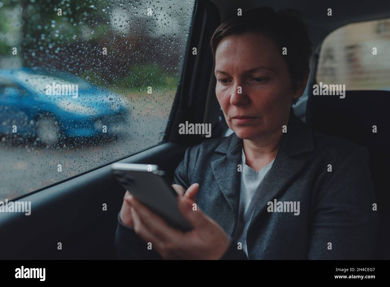 Geschäftsfrau, die bei Regen auf dem Rücksitz des Autos SMS schreibt, selektiver Fokus Stockfoto