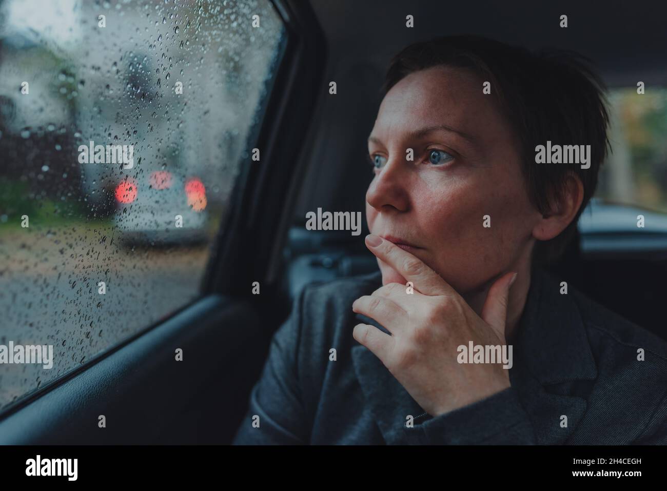 Besorgte Geschäftsfrau, die im Auto wartet und bei Regen aus dem Fenster schaut, selektiver Fokus Stockfoto