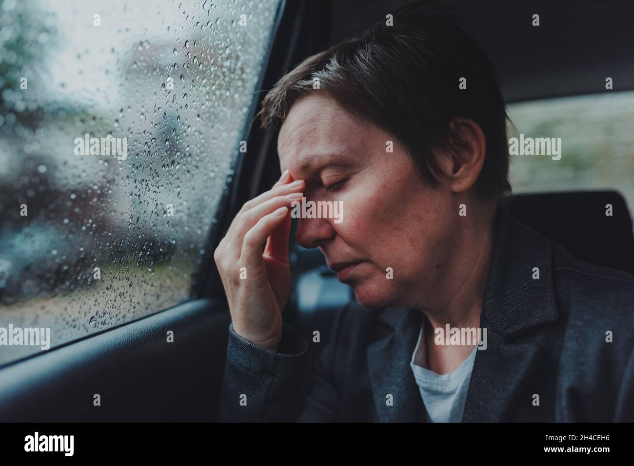 Müde erschöpfte Geschäftsfrau auf dem Rücksitz des Autos bei Regen, selektiver Fokus Stockfoto
